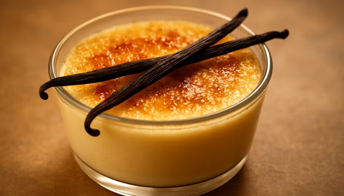 Creamy vanilla bean custard in a glass bowl, garnished with fresh pods and a golden caramelised top.